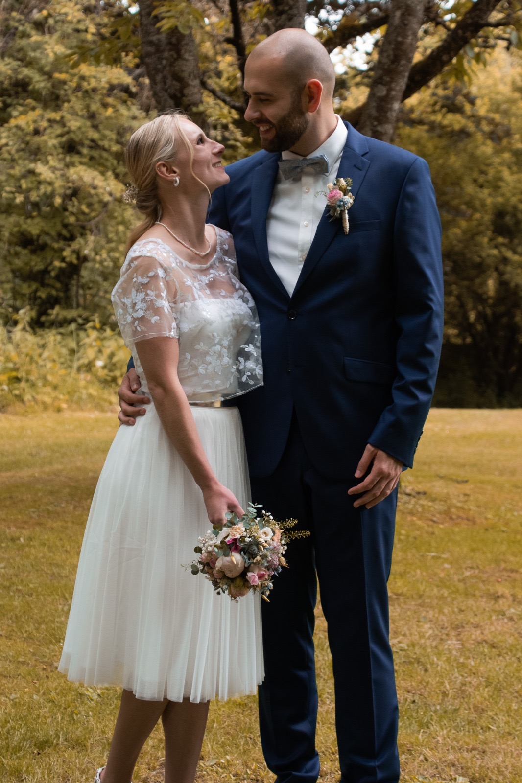 Sophie und Anthony blicken sich lächelnd an, im Hintergrund herbstliches Grün